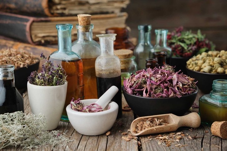 Bottles of healthy tincture or infusion, mortar and bowls of medicinal herbs, old books on wooden table. Herbal medicine.